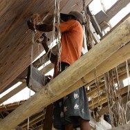 A worker knocking rope and bark between the planks to prevent leaking once it hits the water.