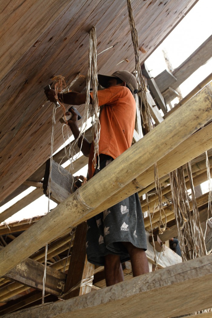 A worker knocking rope and bark between the planks to prevent leaking once it hits the water.